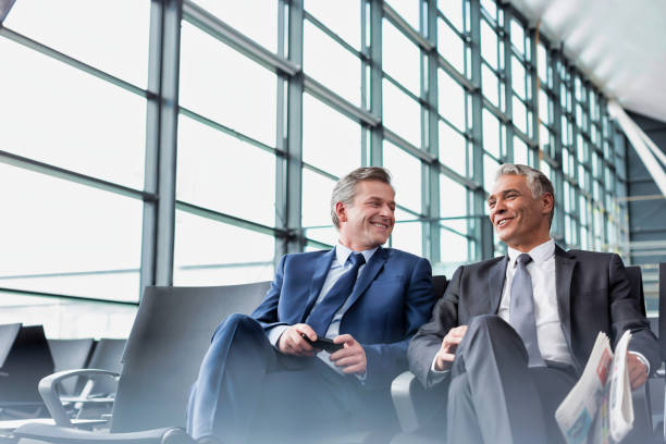 Mature businessmen talking while sitting and waiting for boarding in airport Mature businessmen talking while sitting and waiting for boarding in airport newspaper airport reading business person stock pictures, royalty-free photos & images