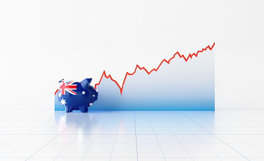 Piggy bank textured with Australian flag sitting in front of a line graph on white background. Horizontal composition with copy space. Volatility in Australian Economy and Australian Dollars.