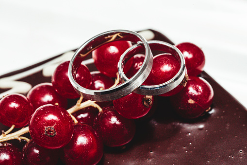 A pair of wedding rings on a bunch of currant lying on chocolate background.