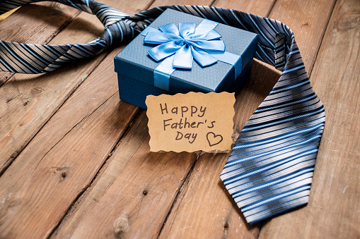 Happy Fathers Day gift box with tie on a rustic wood background. Space for text.