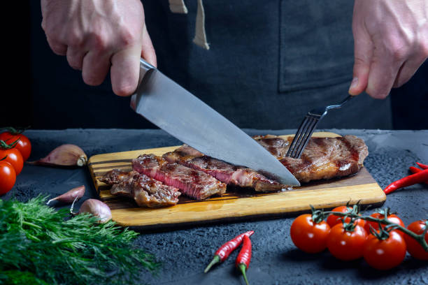 istock A man slices a steak with a knife and fork. Cropped photo with hands closeup. Fresh medium beef steak 1220649580