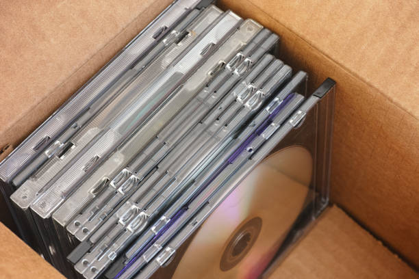 Old collection of DVDs or CDs with some dust on them inside a cardboard box. Close up.