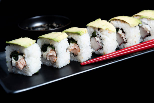 sushi roll with avocado wrap, grilled salmon, philadelphia cheese and green onions on black plate and red chopsticks. small pot with soy sauce. black background. - fine dining grilled spring onion healthy lifestyle imagens e fotografias de stock