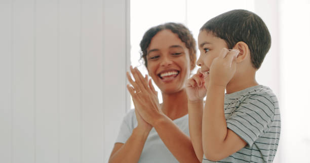 He's flossing on his own! Cropped shot of a mother helping her adorable young son floss his teeth in their bathroom at home dental floss stock pictures, royalty-free photos & images