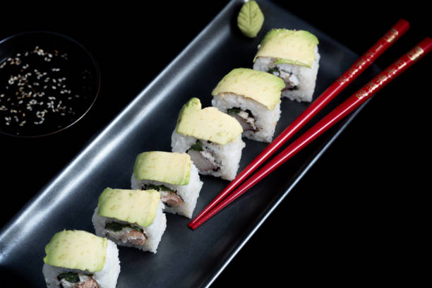sushi roll with avocado wrap, grilled salmon, philadelphia cheese and green onions on black plate and red chopsticks. small pot with soy sauce. black background. - fine dining grilled spring onion healthy lifestyle imagens e fotografias de stock