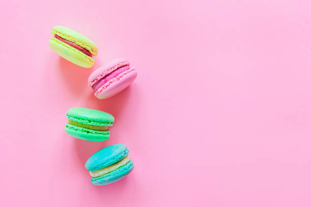 甘いアーモンドカラフルなピンクの青い黄色の緑のマカロンやマカロンデザートケーキは、トレンディなピンクのパステルの背景に分離しました。フランスの甘いクッキー。最小限の食品ベ� - macaroon cake candy variation ストックフォトと画像