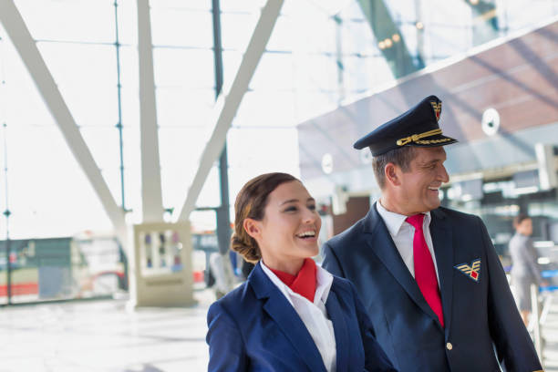 portrait of mature pilot and attractive flight attendant walking while smiling in airport - cabin crew pilot airport walking imagens e fotografias de stock