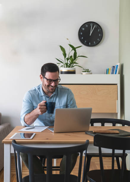istock Happy smiling young man watching and working on computer laptop at home and drinking coffee or tea stock photo 1220656201