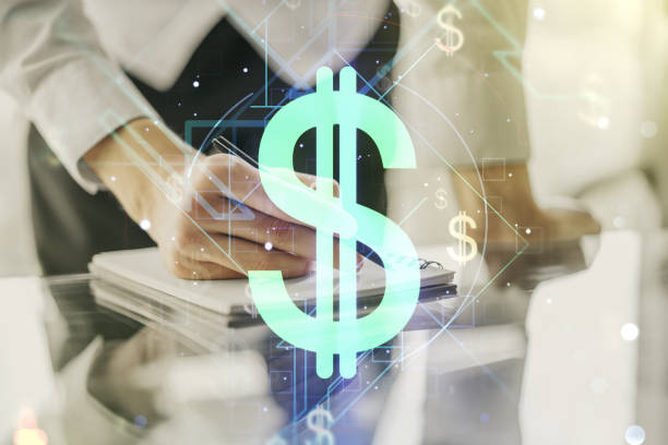 istock Double exposure of creative USD symbols hologram and man hand writing in diary on background. Banking and investing concept 1220657334