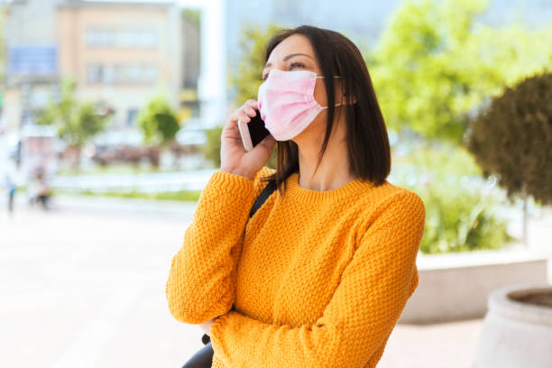 istock Young Woman With Face Mask Using Smart Phone Talking 1220665825