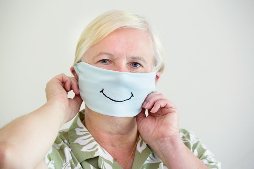 COVID-19, a senior adult woman with a homemade face mask for Social Distancing. Studio portrait on neutral gray background.