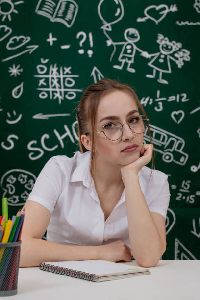 istock Young teacher is sitting near blackboard in classroom 1220667745
