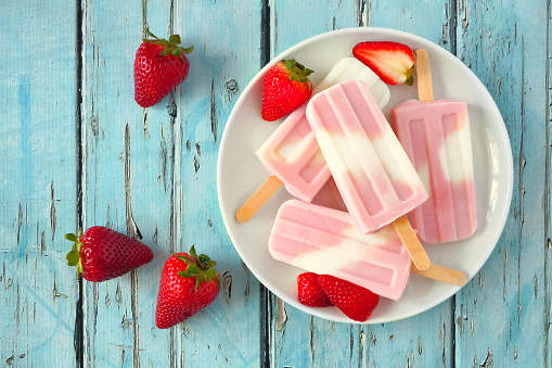 Healthy strawberry yogurt summer popsicles on a plate, top view table scene against a blue wood background