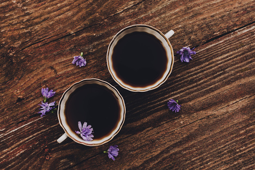 Lilac chicory flowers and cups on vintage wooden table. Flat lay, copy space. Natural coffee substitute.