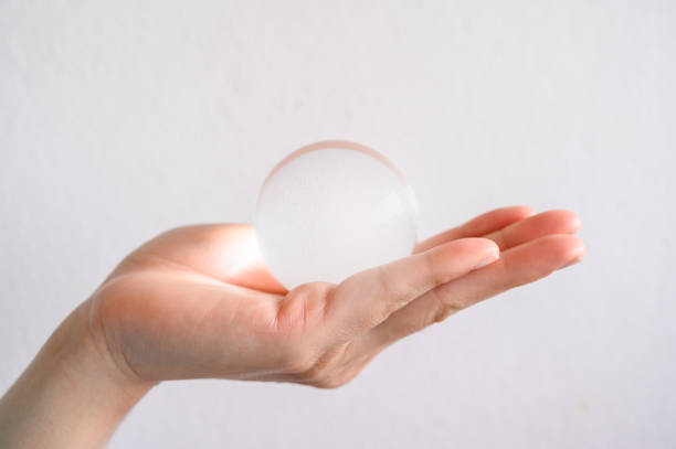 fermez-vous vers le haut de la main de quelqu’un retenant une boule transparente claire de cristal. - transparent crystal crystal ball human hand photos et images de collection