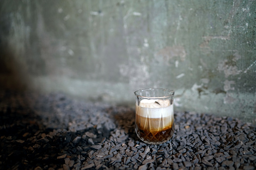 Iced black coffee with milk - A glass of cold brew coffee topped with milk foam on gravel background.