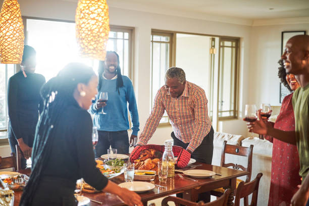 homme servant la dinde tandis que la famille appréciant à la maison - thanksgiving dinner party turkey feast day photos et images de collection