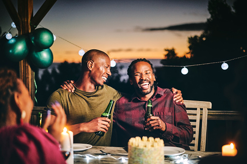 Cheerful male friends enjoying beer together. Men and woman are sitting at table. They are having fun in birthday party at night.