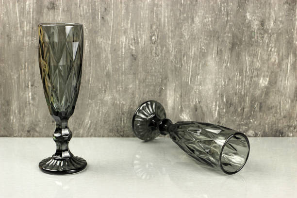 istock Dark champagne glasses on a grey background.One is standing, the other has fallen 1220700252