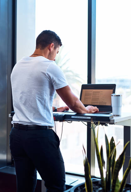 Take your standing desk to the next level Shot of a young businessman working on a laptop while walking on a treadmill in an office standing desk photos stock pictures, royalty-free photos & images