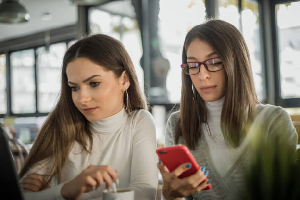 istock Two girls are sitting at a cafe and having fun using laptops and mobile phones 1220705321