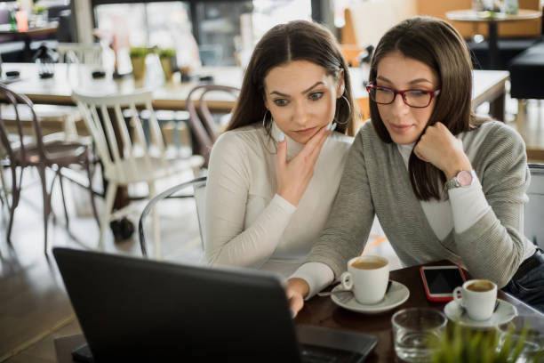 istock Two girls are sitting at a cafe and having fun using laptops and mobile phones 1220705384