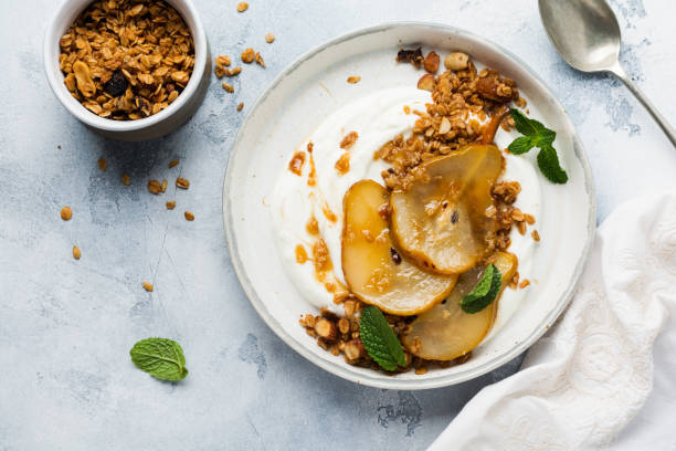 istock Greek yogurt with caramelized pear, granola, nuts and melted sugar for a wholesome breakfast on a gray ceramic plate. Rustic style. Top view. 1220705482