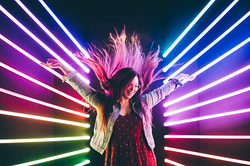 Attractive dancing girl, hair flying, neon light. Portrait of girl posing with hands up.