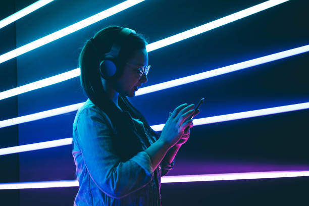 istening electronic music Woman in headphones listening music in neon light with phone on hands. mobile phone lights up stock pictures, royalty-free photos & images