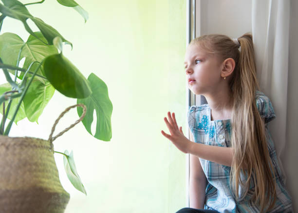 istock Sad child girl by the window 1220708909