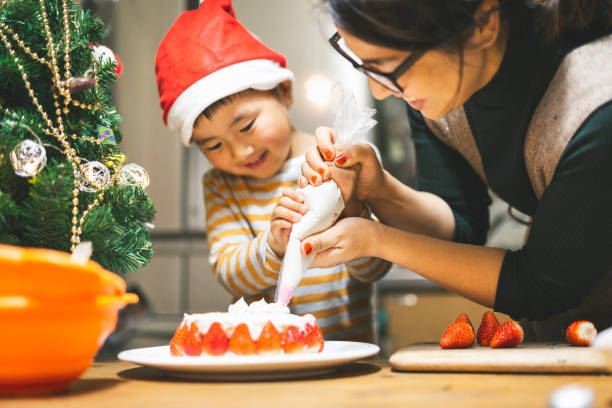 Mother and son making Christmas cake together Asian mother and son decorating Christmas cake at home. christmas cake stock pictures, royalty-free photos & images