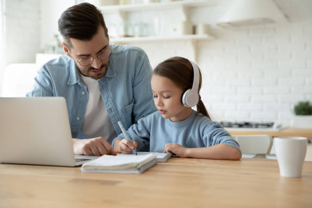 思いやりのあるお父さんと娘は自宅でオンラインビデオクラスを持っています - two parent family indoors home interior domestic kitchen ストックフォトと画像