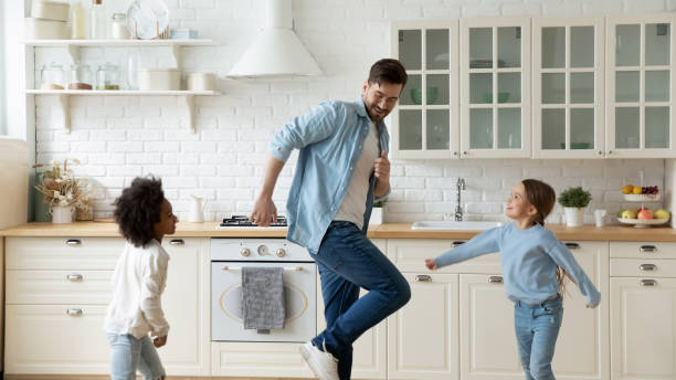 istock Caucasian father dance in kitchen with excited multiethnic daughters 1220716946