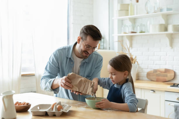 Caring dad and small daughter baking in kitchen together Caring young Caucasian father and cute little preschooler daughter bake in kitchen at home together, happy loving dad teach small girl child cooking, preparing pancakes or biscuits for breakfast pancake photos stock pictures, royalty-free photos & images