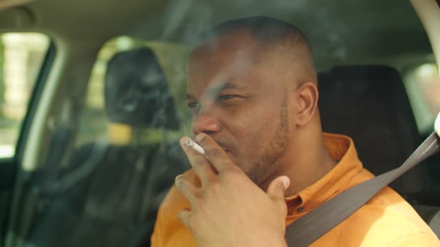 Nervous african male driver smoking cigarette in car