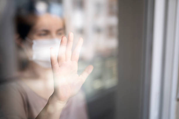 istock Young woman in quarantine looking through the window 1220721350