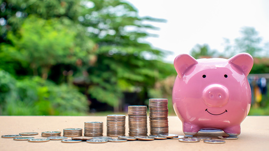 Stack coins that are arranged in ascending order, including piggy bank for saving with a green background blur, ideas for saving money and financial growth.