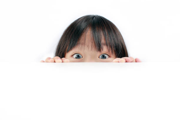 Little girl peeking over table Portrait of little Asian girl looking at the camera over the table isolated on white background peeking stock pictures, royalty-free photos & images
