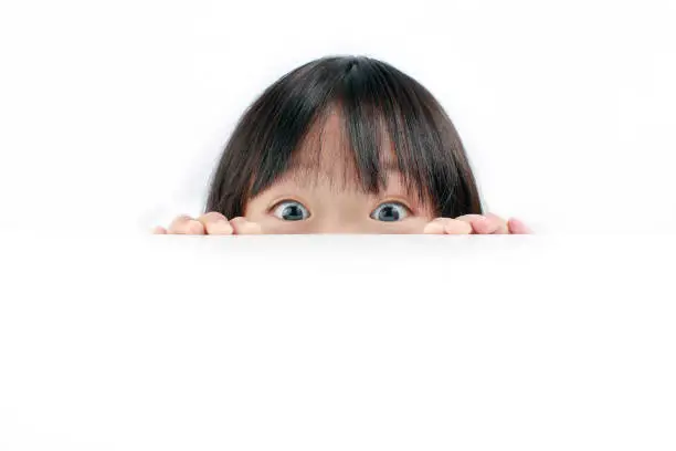 Portrait of little Asian girl looking at the camera over the table isolated on white background