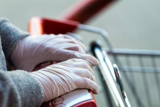 istock Hands wearing protective surgical gloves pushing shopping trolly at supermarket 1220729310