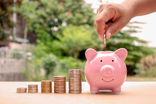 Close-up of a woman putting a coin in a piggy bank, including a coin stack, saving ideas and financial growth.