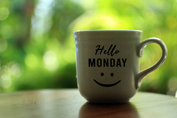 Coffee cup and Hello Monday greeting with an happy big smile emoticon on it, on fresh light green background. Copy space for your text or design. Monday morning coffee concept.