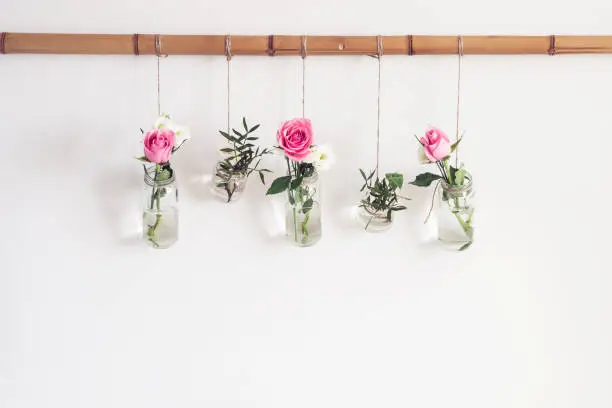 DIY stylish holiday decoration. Flowers in vases jars are suspended from white wall in room. Seasonal romantic decoration, front view.