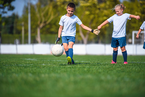 Surface level view of 7 and 8 year old boy and girl footballers practicing on sports field.