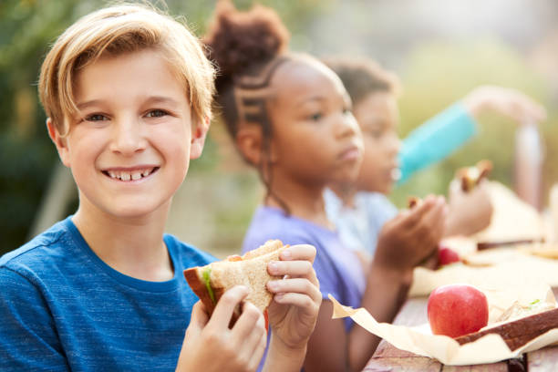 portret chłopca z przyjaciółmi jedzenie zdrowego pikniku na zewnątrz tabeli na wsi - apple eating little girls green zdjęcia i obrazy z banku zdjęć