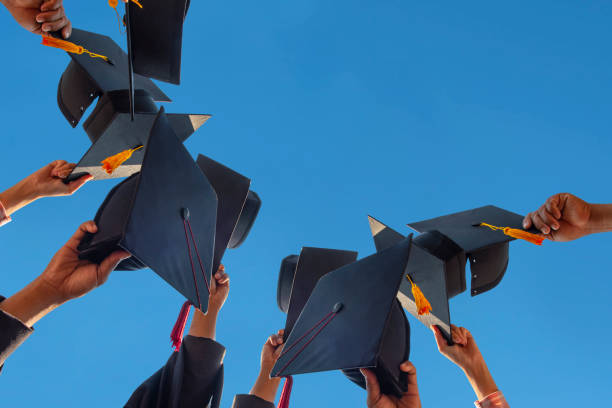 les étudiants retenant un coup de chapeau de graduation par leur main dans un ciel lumineux pendant les diplômés de succès de cérémonie à l’université, concept de l’éducation réussie dans l’école de secondaire, diplôme félicité - graduation color image people photography photos et images de collection