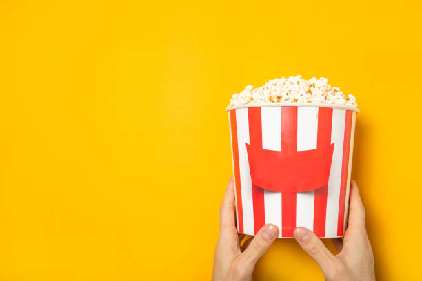 istock The guy holds popcorn in his hands on a yellow background. Place for text. 1220732943