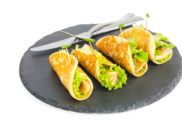 istock Pancake rolls with fish and lettuce. Salmon bread roll with cheese. On black stone plate. 1220736977