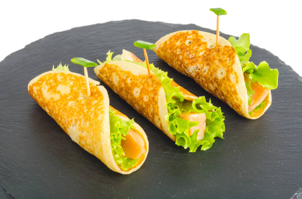 istock Pancake rolls with fish and lettuce. Salmon bread roll with cheese. On black stone plate. 1220736978