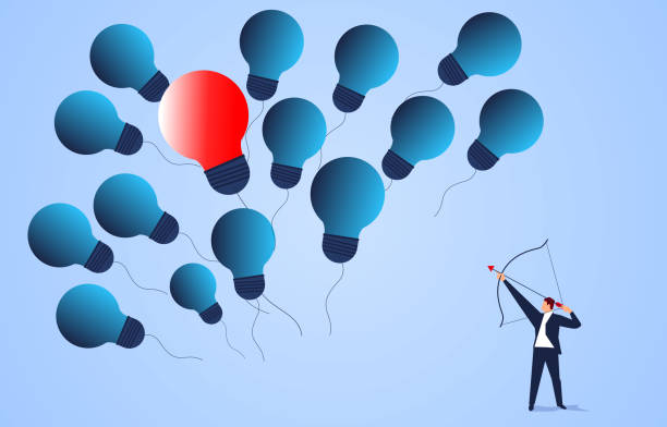 istock Businessman holding a bow and arrow shooting a red lightbulb in the middle of a group of flying lightbulbs 1220737786